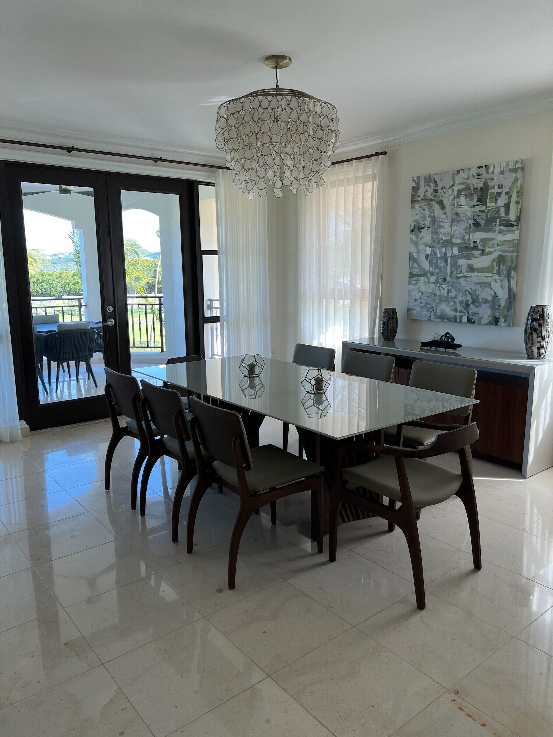 A dining area with a large table, chairs, a chandelier, and a view of the outdoors.