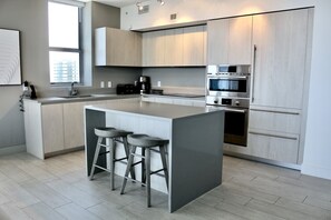 A modern kitchen with a central island, bar stools, stainless steel appliances, and light wood cabinetry.