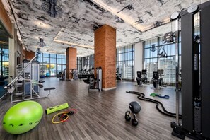 A spacious gym with various exercise equipment, large windows, and a wooden floor.