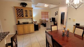 A dining area with a wooden table and chairs, a kitchen with wooden cabinets, and a living room with a sofa and a TV. - Pet Friendly - Overlooks Pool - Sleeps Tons (South Padre Island)