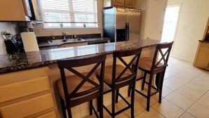 A kitchen with a granite countertop, wooden chairs, a stainless steel refrigerator, and wooden cabinets. - Pet Friendly - Overlooks Pool - Sleeps Tons (South Padre Island)