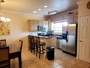 Una cocina con una mesa, sillas, un cubo de basura y un refrigerador.
