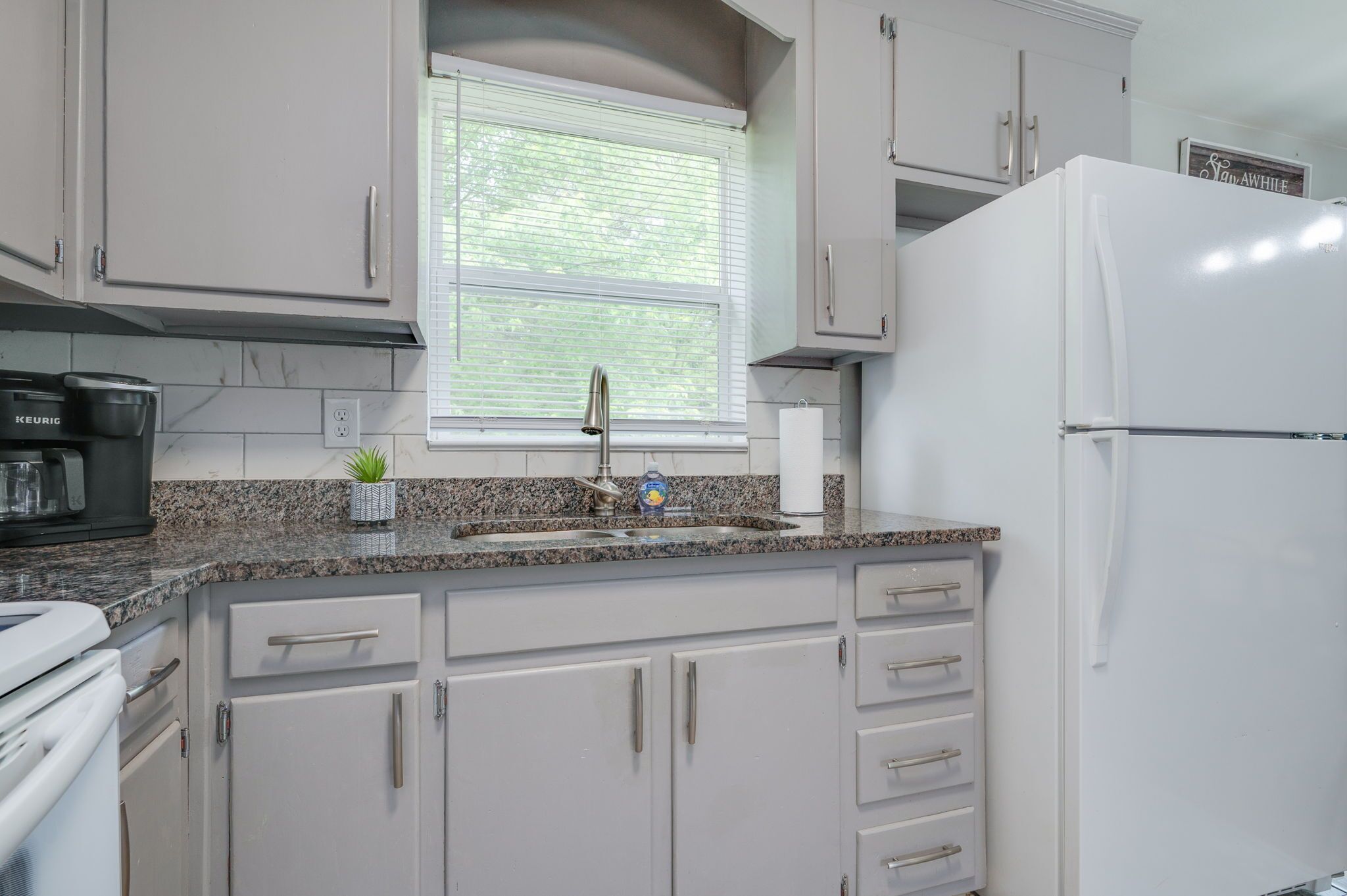 A kitchen with white cabinets, a granite countertop, a stainless steel faucet, and a white refrigerator.