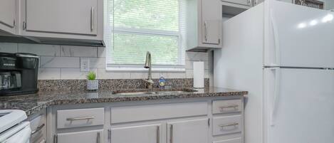 A kitchen with white cabinets, a granite countertop, a stainless steel faucet, and a white refrigerator.