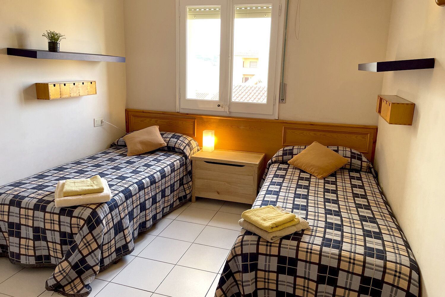 A bedroom with two beds, a nightstand, a window, and built-in shelves.