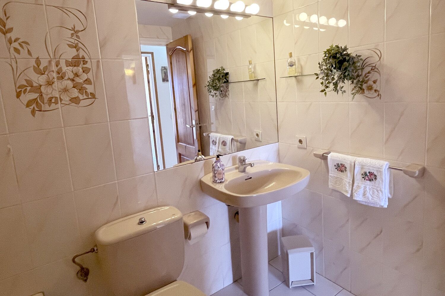 Un baño con inodoro, lavamanos, espejo y toallero.