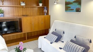 A living room with a sofa, TV, wooden cabinets, and decorative items. - Apartment in Clota Petita, L´Escala, 2 minutes from the beach! (L'Escala)