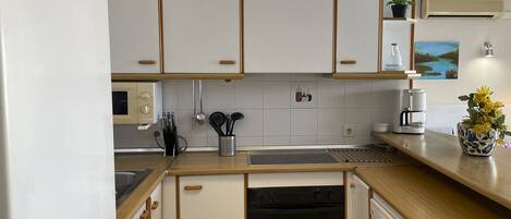 A modern kitchen with white cabinets, a built-in oven, a dishwasher, and a coffee maker.
