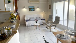 A modern living room with a sofa, two chairs, a coffee table, and a dining area with a table set for two. - Apartment in Clota Petita, L´Escala, 2 minutes from the beach! (L'Escala)