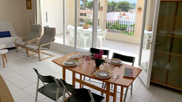 A dining area with a table set for four, a sofa, and a balcony with outdoor seating. - Apartment in Clota Petita, L´Escala, 2 minutes from the beach! (L'Escala)