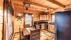 A wooden cabin interior with a dining table, chairs, a refrigerator, wooden cabinets, and a kitchen area. - New log cabin, Smoking views of the Smoky Mountains! (Bryson City)