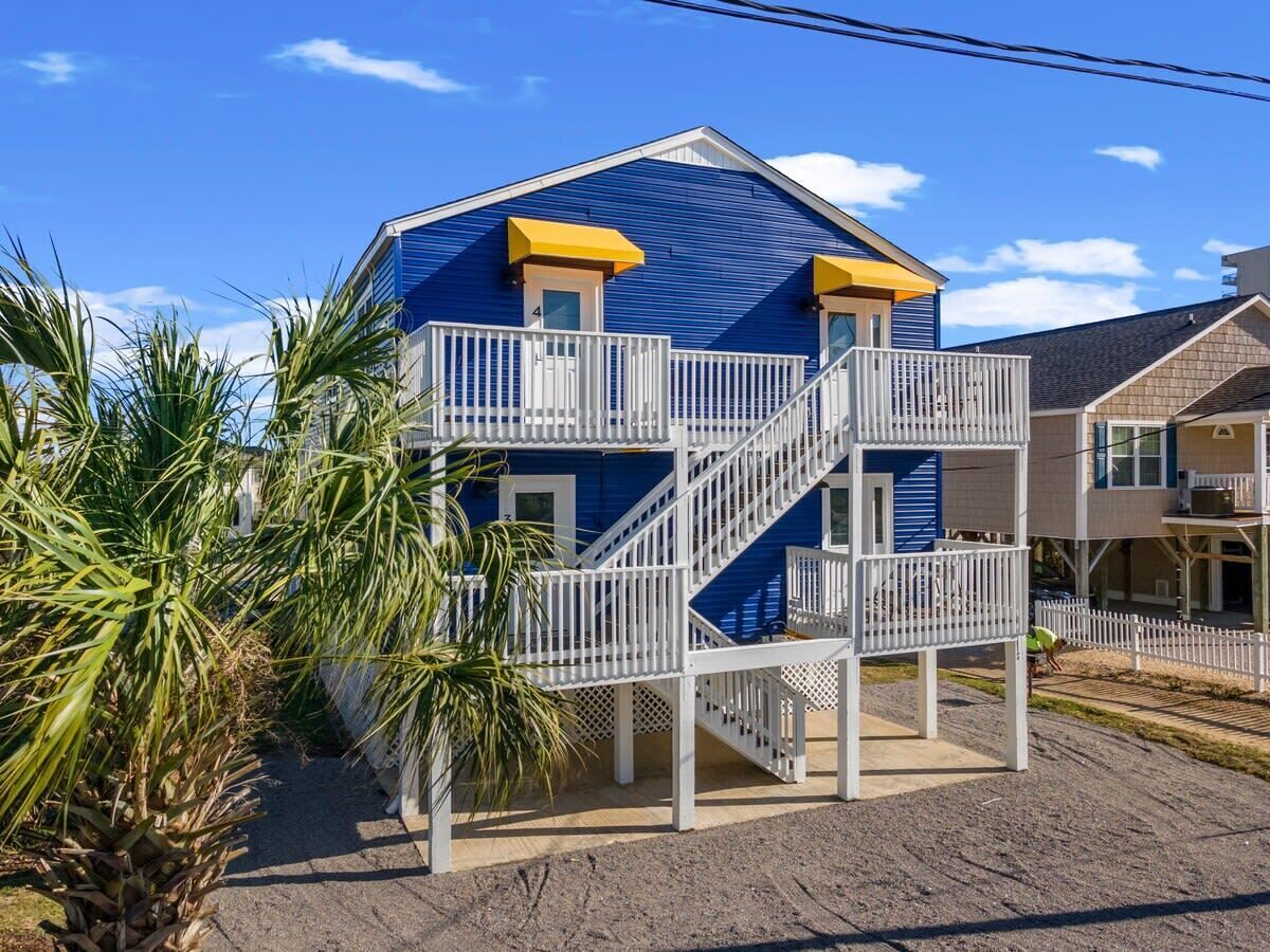 A two-story house with a blue exterior and white railings, featuring a central staircase and a small balcony.