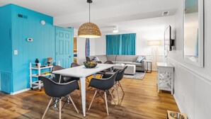 A modern living room with a white dining table, black chairs, and a woven pendant light.