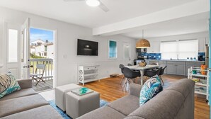 A modern apartment with a living room, dining area, and kitchen. There is a balcony with a view of neighboring houses.