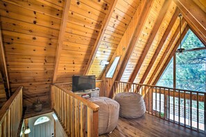 A wooden interior with a TV, seating, and a balcony with a view.
