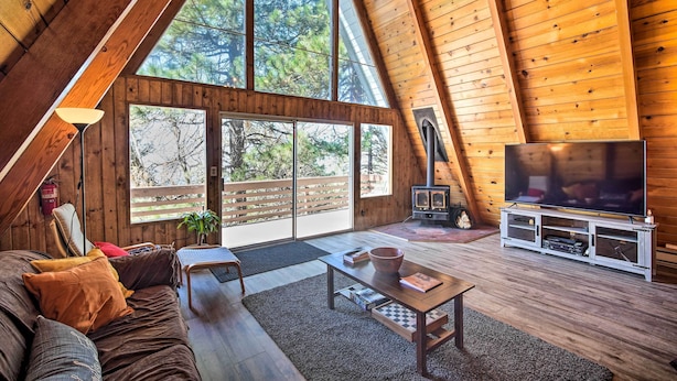 A spacious loft with a high ceiling, large windows, a cozy seating area, and a fireplace. - Running Springs Cabin w/ Large Deck + View! (Running Springs)