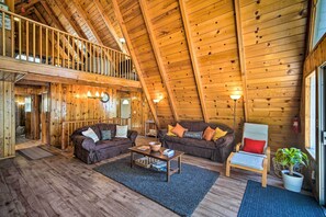 A spacious loft-style room with wooden walls and a sloped ceiling, furnished with two sofas, a coffee table, and a chair.