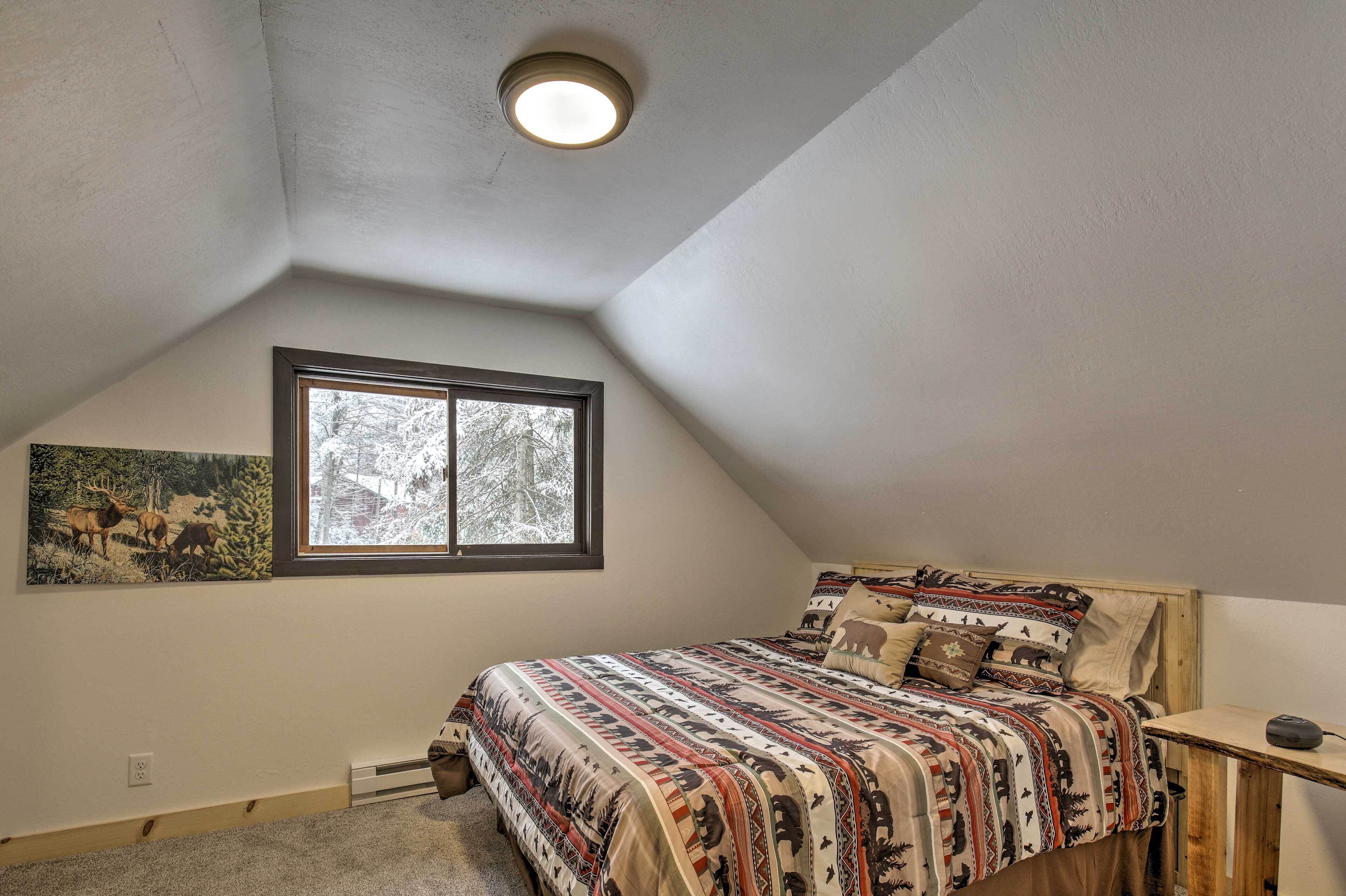 Een slaapkamer met een schuine balklaag, een raam met uitzicht op bomen, een bed met beddengoed met een patroon, en een wandradiator.