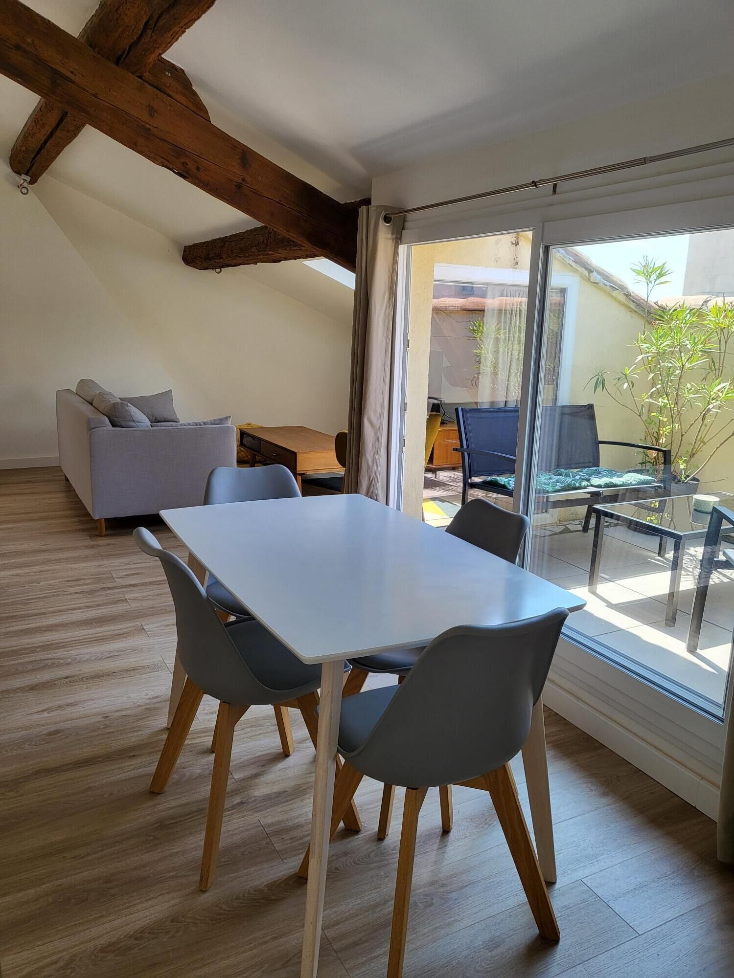 Un salon moderne doté d’une grande table à manger, de chaises grises, d’un canapé et d’une porte vitrée donnant sur un espace extérieur avec une table et des chaises.