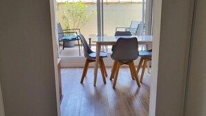 A room with a wooden floor, a table with chairs, and a view through a glass door to an outdoor area with chairs and a plant. - La Dolce Vita Nîmoise 🐊 Terrace 100 m from the Arena (Nîmes)
