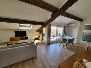 Un salón tipo loft con techo de madera, un sofá, un televisor y un comedor con mesa y sillas.