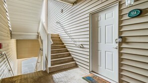 Un escalier en bois mène à une porte blanche ornée d’une plaque portant un numéro.