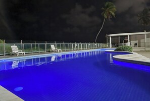 A swimming pool with a curved edge, a fence, and a few lounge chairs.