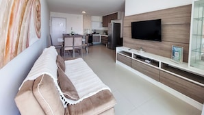 Una sala de estar moderna con un sofá, televisión y un comedor al fondo.