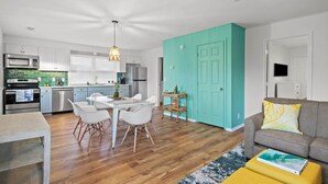 A modern kitchen with white cabinets, a dining table with white chairs, and a teal accent wall. - Beach Nest 4 Stylish 2Min Walk to Beach (North Myrtle Beach)