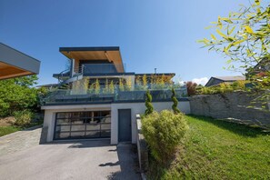 Ein modernes, zweistöckiges Haus mit Glasbalkon, Garage und einer Mauer aus Naturstein.