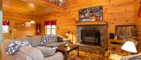 A cozy cabin interior with a fireplace, a sofa, and a television mounted above it.