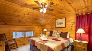 A cozy wooden cabin bedroom with a bed, a rocking chair, a nightstand, and a ceiling fan. - Rustic Cabin With Mountain Views (Todd)
