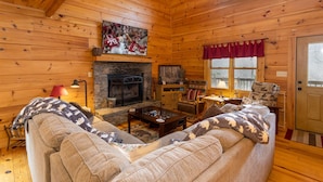 A cozy log cabin interior with a fireplace, a television mounted above it, and a comfortable seating area with a sofa and armchairs. - Rustic Cabin With Mountain Views (Todd)