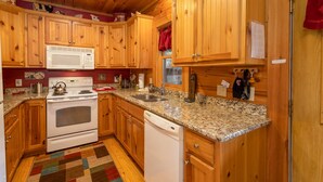 A kitchen with wooden cabinets, a microwave, stove, and granite countertops. - Rustic Cabin With Mountain Views (Todd)
