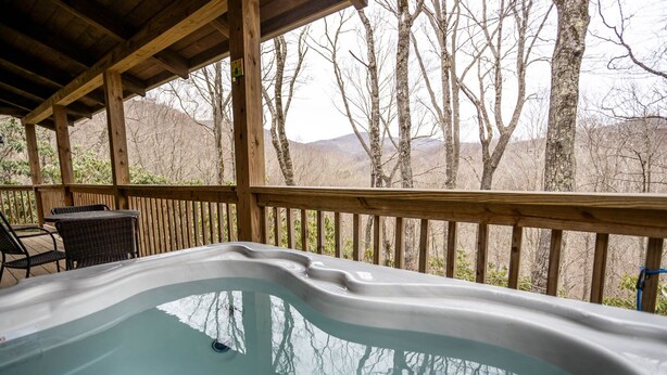 A hot tub under a wooden deck with a view of trees and mountains. - Rustic Cabin With Mountain Views (Todd)