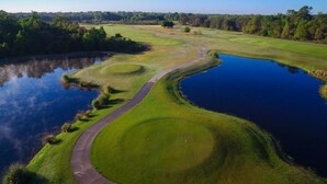 A golf course with a pond, pathways, and surrounding trees. - Pool Home in Gated Golf Community With Game Room & Themed Kid's Rooms (Davenport)