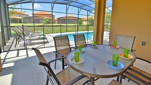 A covered patio with a table and chairs, a pool in the background, and a view of houses. - Pool Home in Gated Golf Community With Game Room & Themed Kid's Rooms (Davenport)