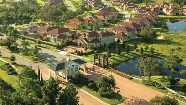 A residential area with houses, a central driveway, and a small body of water. - Pool Home in Gated Golf Community With Game Room & Themed Kid's Rooms (Davenport)