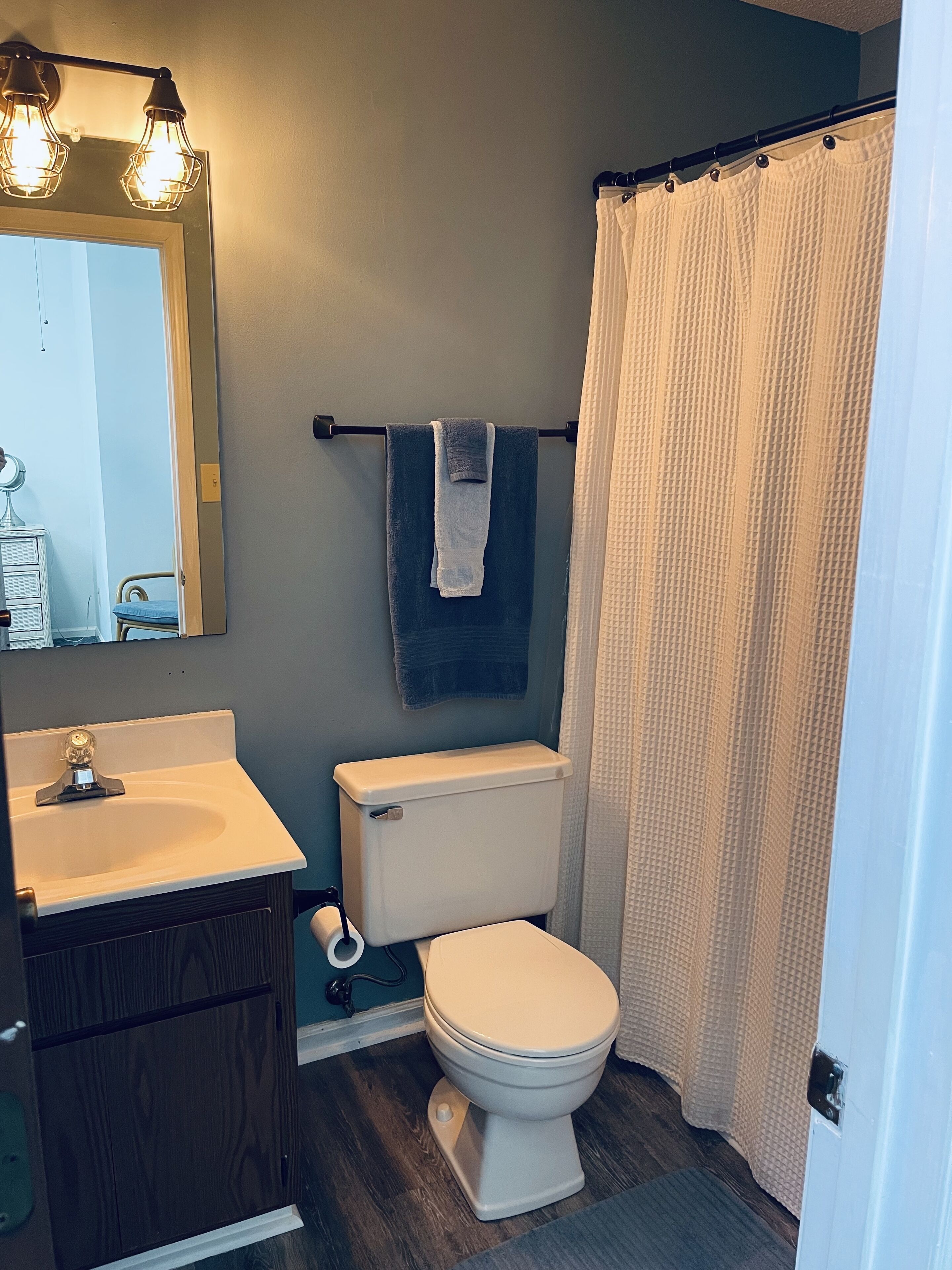 A bathroom with a toilet, sink, mirror, and towel rack.