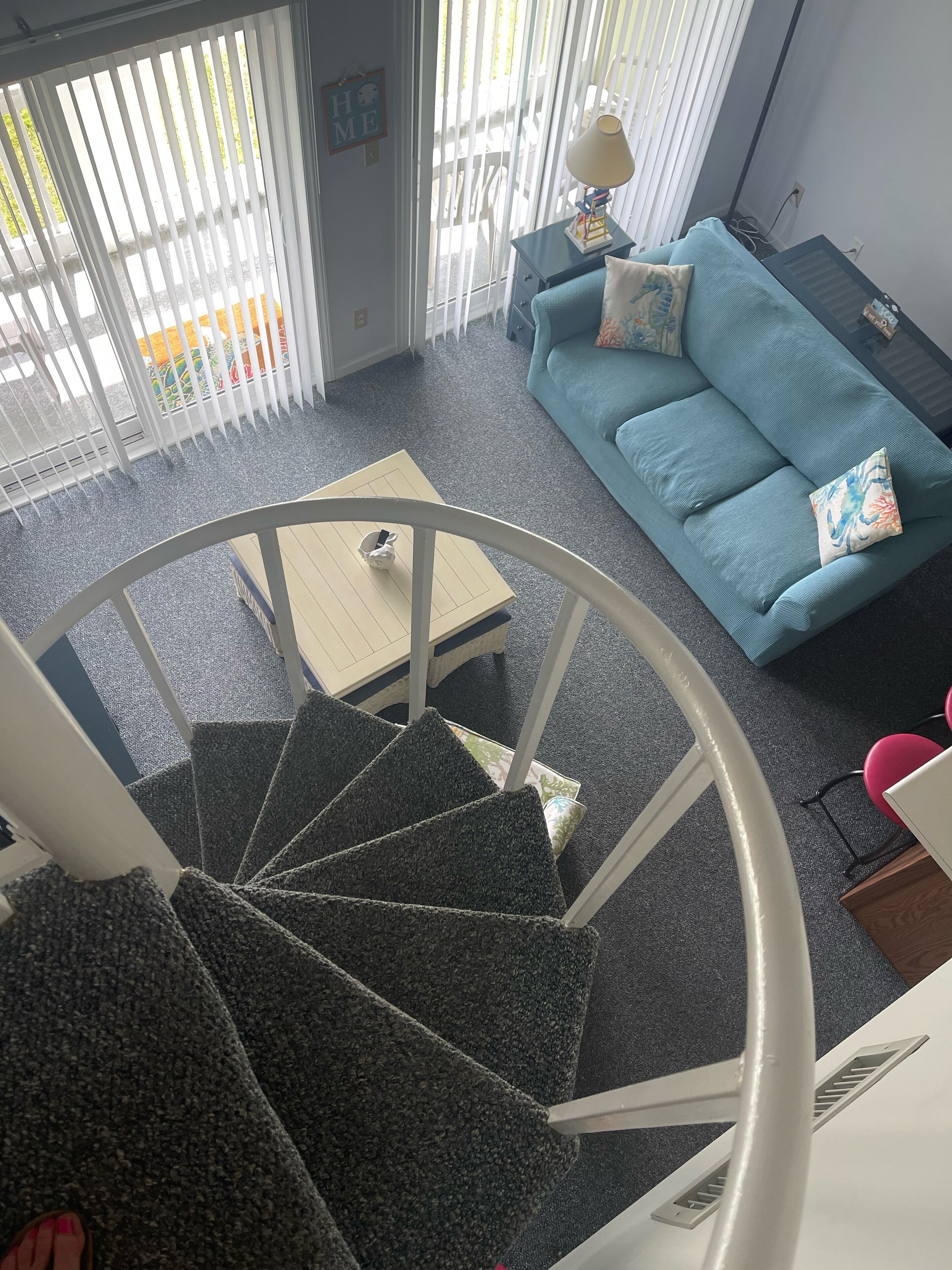 Un salón con un sofá azul, una mesita y una escalera.