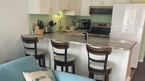 Een compacte keuken met witte kasten, een centraal eiland en een zithoek met een blauwe bank en houten stoelen.