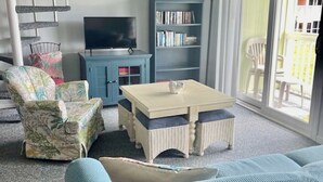 Een woonkamer met een bank, een bijzettafeltje, een televisie, een boekenkast en een spiltrap.