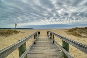 Een houten vlonder die naar een zandstrand leidt, met een bewolkte lucht.