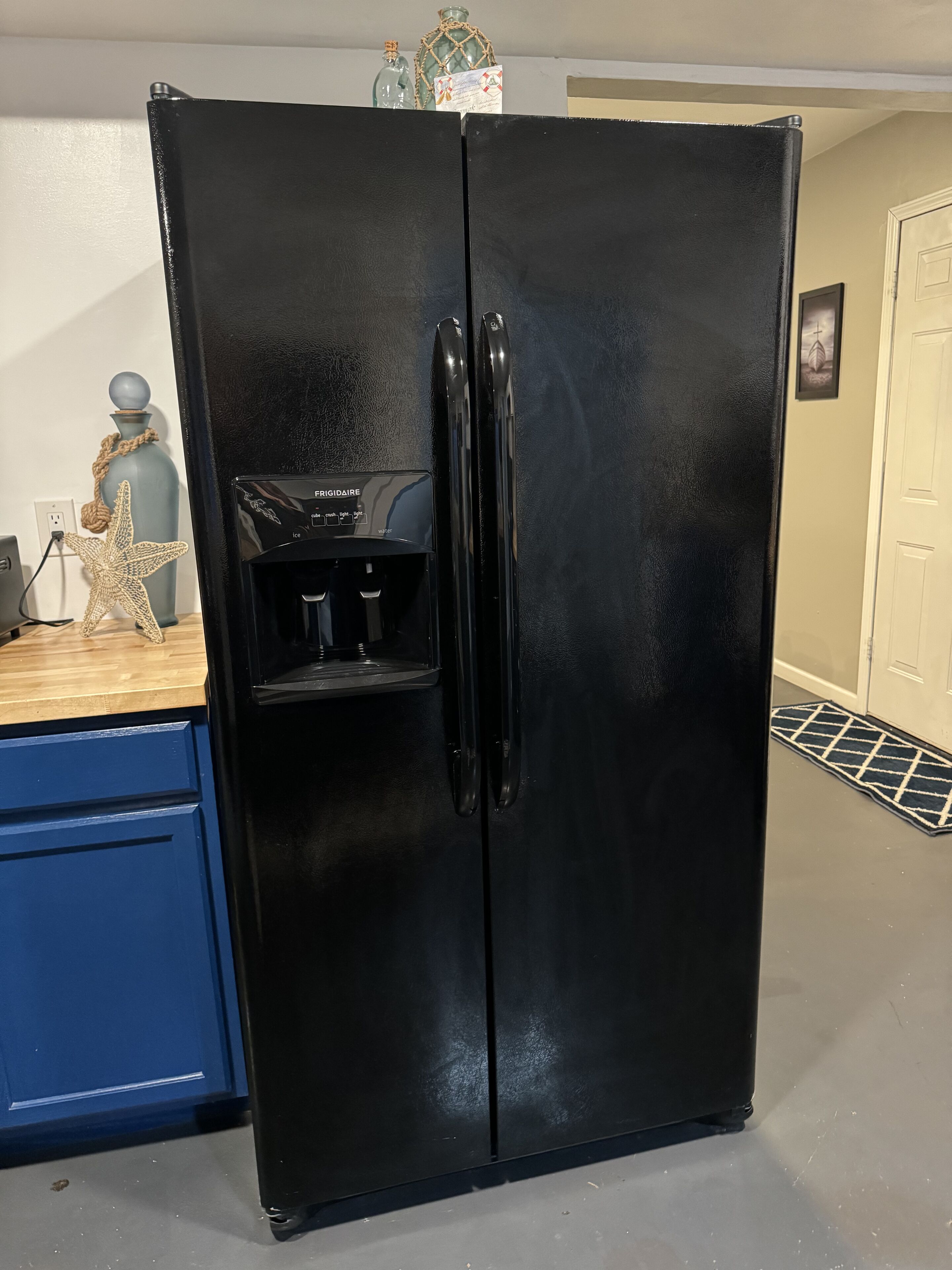 A black refrigerator with a water dispenser, a blue cabinet, and a starfish decoration on the counter.
