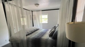 Un dormitorio con cama, mesita de noche, lámpara y cortinas traslúcidas.