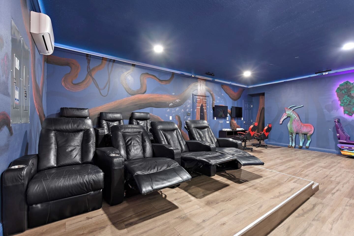 A room with multiple black leather reclining chairs, a wooden floor, and a wall with a wavy design.