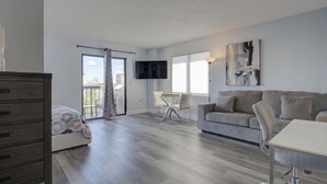 Een ruime woonkamer met een bank, een eettafel en een aan de muur bevestigde televisie.