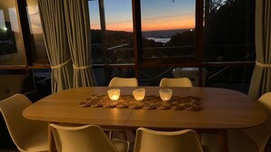 Une table à manger éclairée à la bougie, avec vue sur le coucher de soleil à travers de grandes fenêtres.