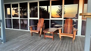 Une terrasse en bois avec deux fauteuils Adirondack et une petite table, offrant une vue panoramique à travers de grandes fenêtres.