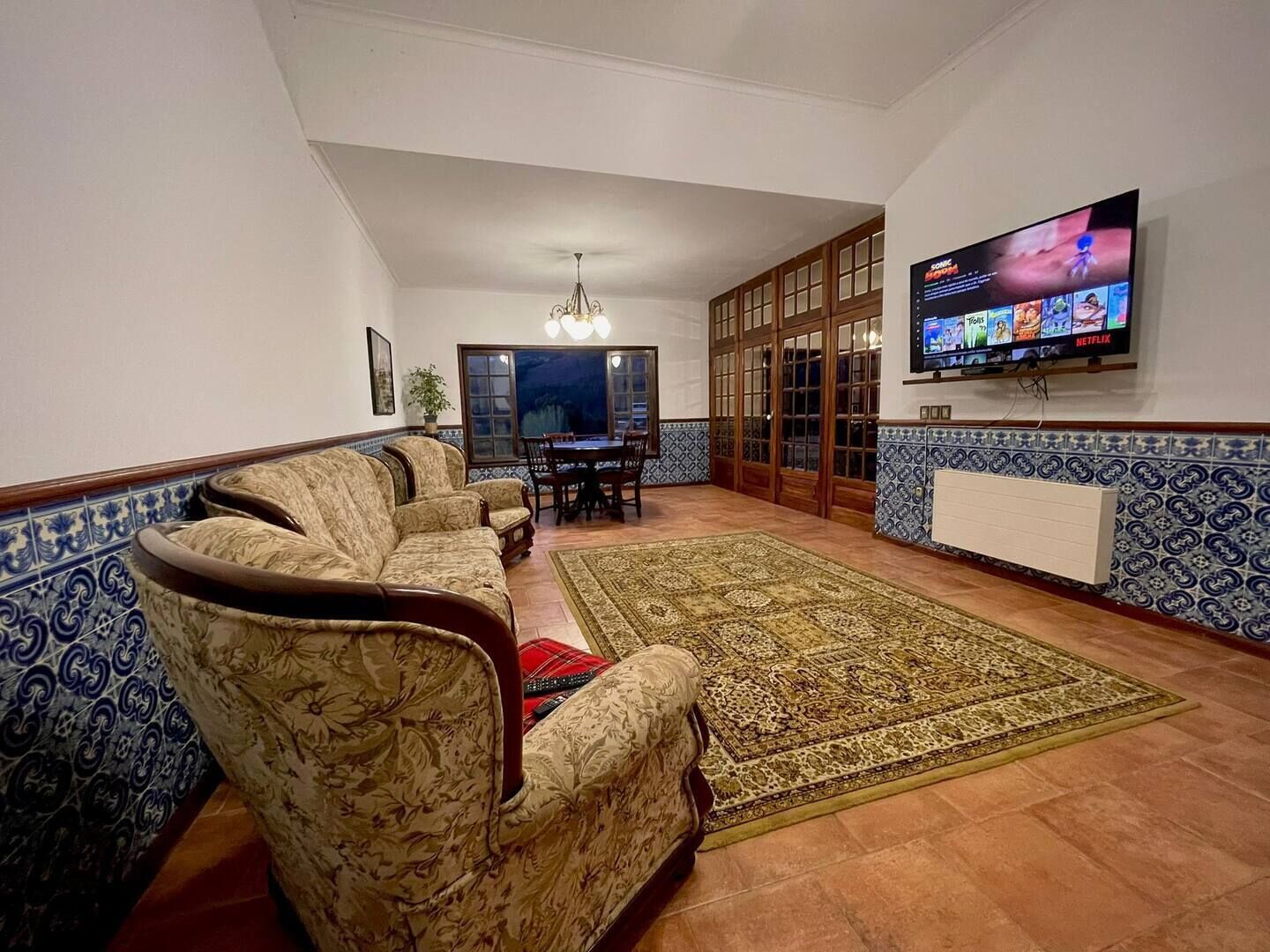 Una sala de estar con sofá, televisor montado en la pared y comedor con mesa y sillas.